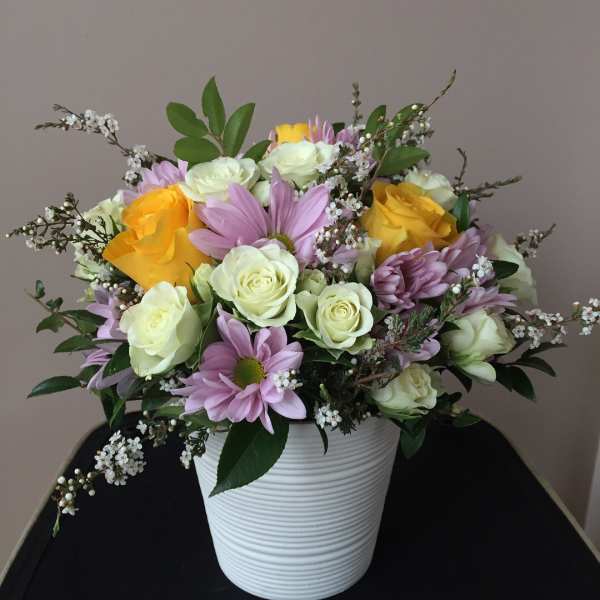Mixed bouquet of yellow and white roses with lavender daisies in a white vase