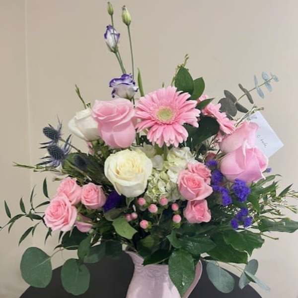 Pink and white mixed flower arrangement with purple accents in a pink ceramic pitcher.
