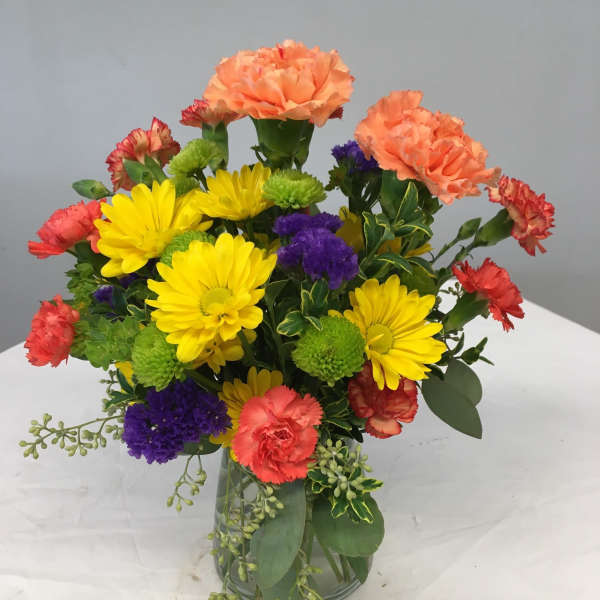 Mixed bouquet of yellow daisies, carnations, and purple blooms in a glass vase