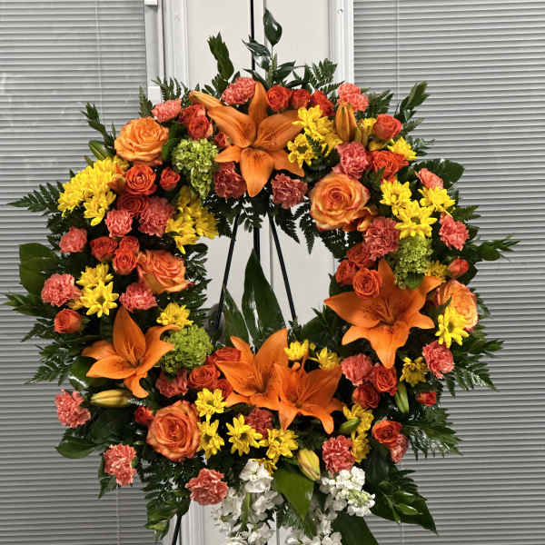 Large floral wreath with orange lilies, roses, and yellow blooms on a stand