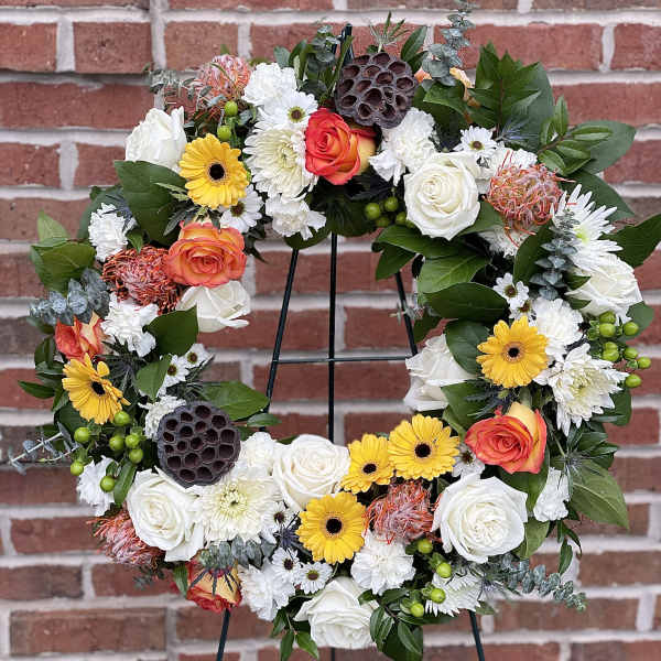 Floral wreath with white, yellow, and orange blooms on a black stand