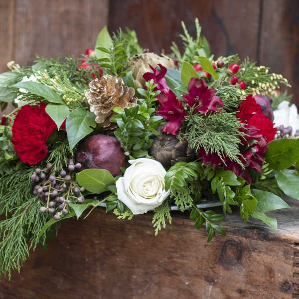 Holiday floral arrangement with red blooms and a white rose in a wooden box