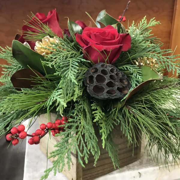 Red roses arranged with evergreen foliage and berries in a wooden box