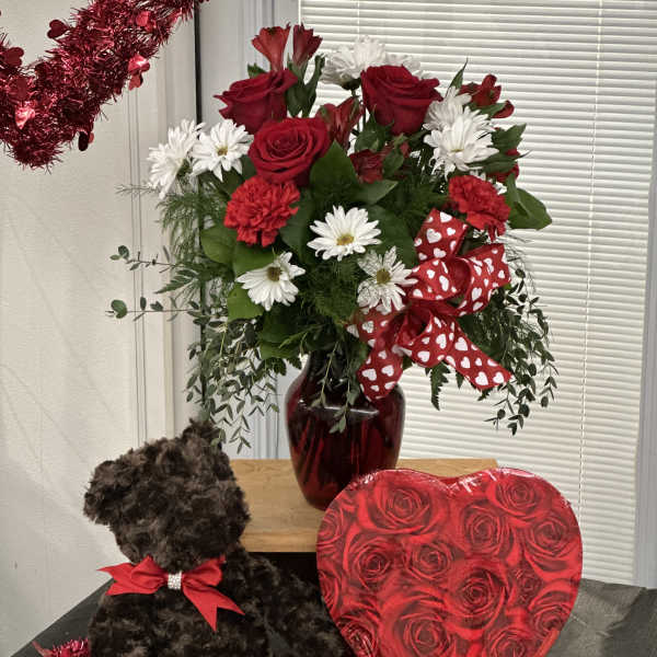 Red roses and white daisies in a vase with a teddy bear and heart box