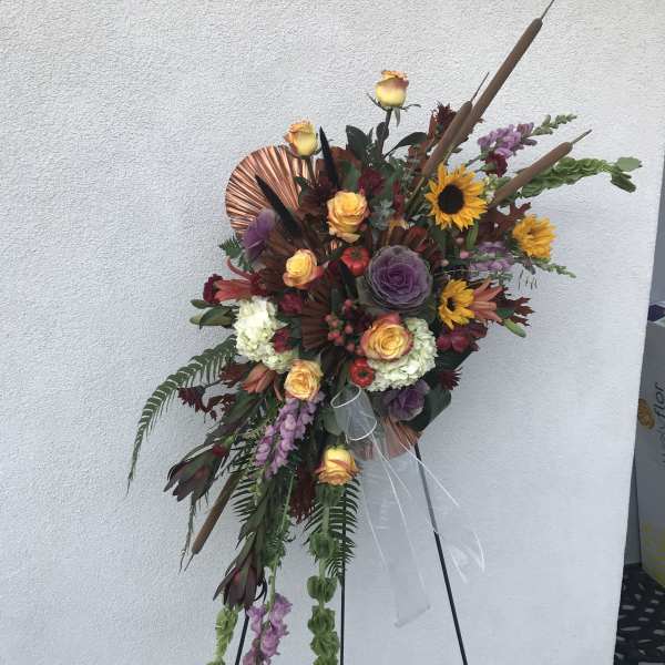 Tall floral standing spray with roses, sunflowers, and purple blooms