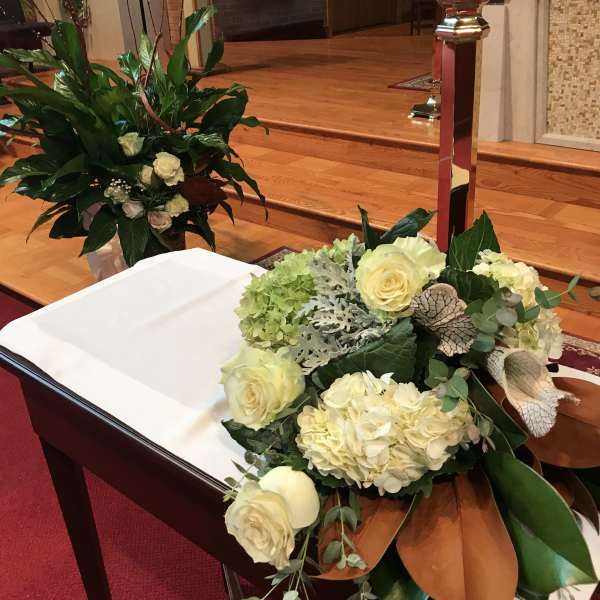 Cream floral arrangement on a church altar beside a white-draped casket