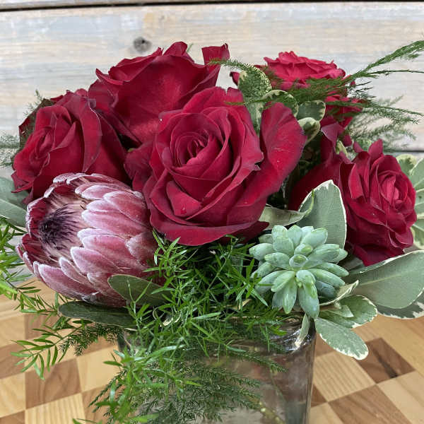 Red roses and a protea in a square glass vase