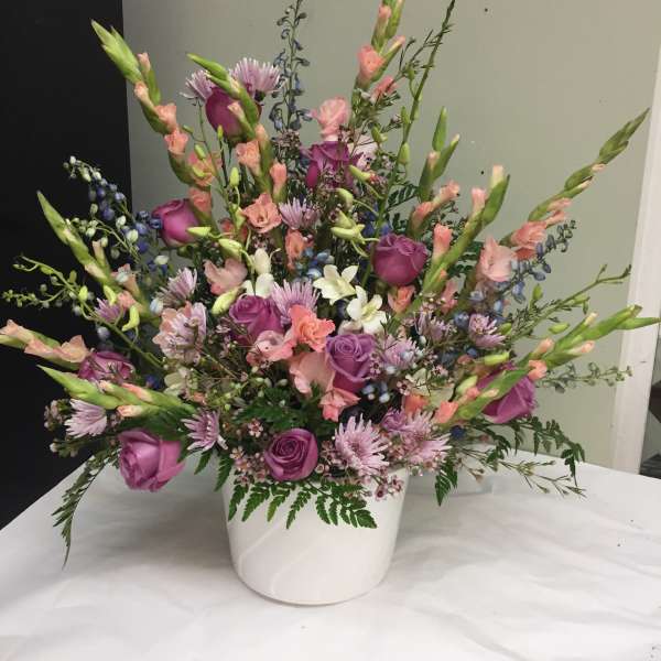 Mixed pink and purple floral arrangement in a white container