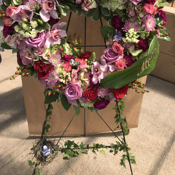 Heart-shaped floral wreath with pink, purple, and red flowers on a stand