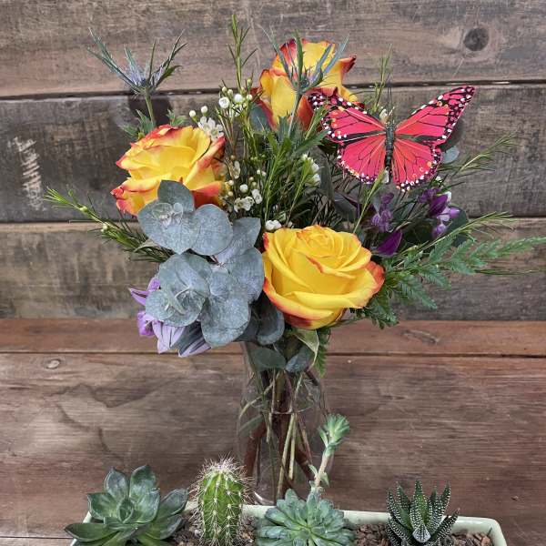 Yellow roses in a glass vase with succulents in a rectangular planter