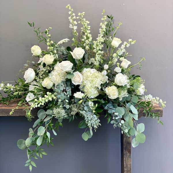 Large white and green floral arrangement with roses and hydrangeas on a wooden stand