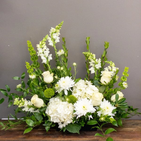 Low white and green floral arrangement with roses, hydrangeas, snapdragons, and mums in a rectangular container