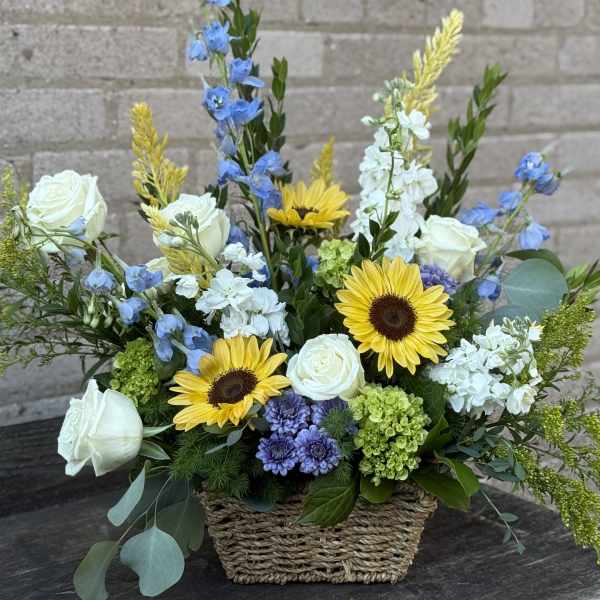 Basket arrangement with white roses, sunflowers, and blue flowers