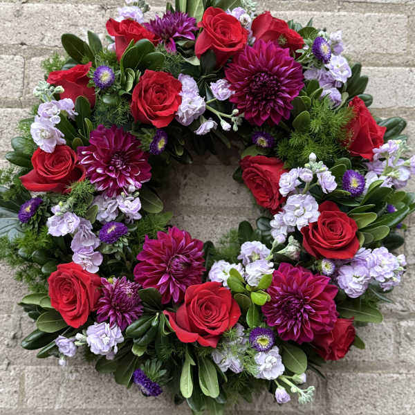 Circular wreath of red roses, purple dahlias, and lavender blooms