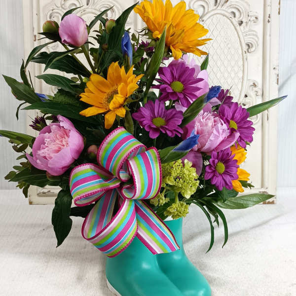 Colorful bouquet in a turquoise rain boot vase with a striped ribbon