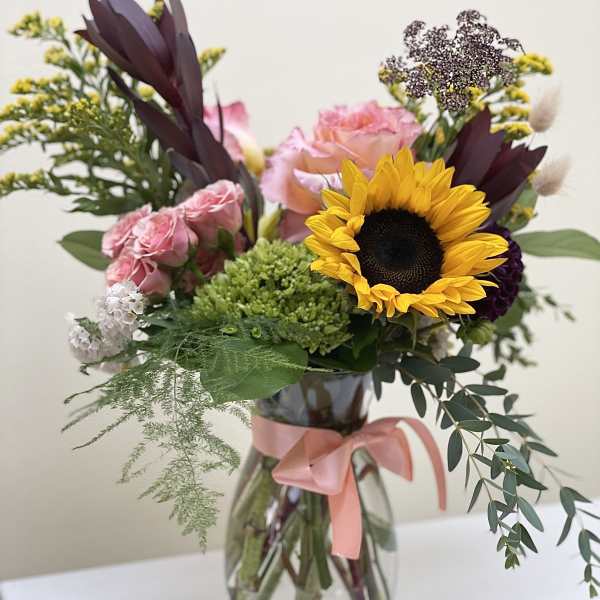 Mixed bouquet with a sunflower, pink roses, and a glass vase tied with ribbon