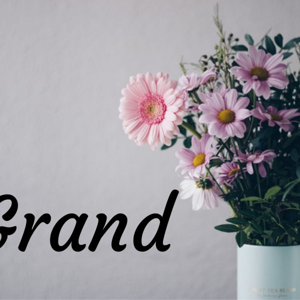Pink and lavender daisies in a light blue vase with the word Grand