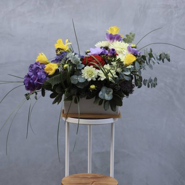 Colorful mixed flower arrangement in a rectangular container on a stand