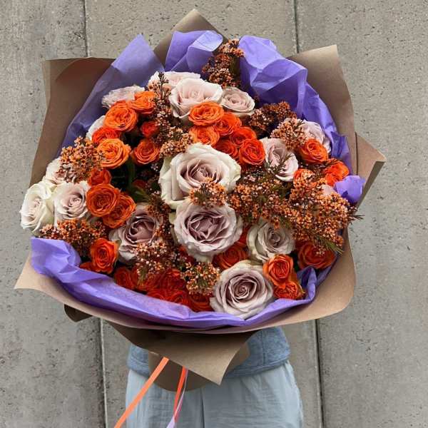 Bouquet of orange and blush roses wrapped in purple paper