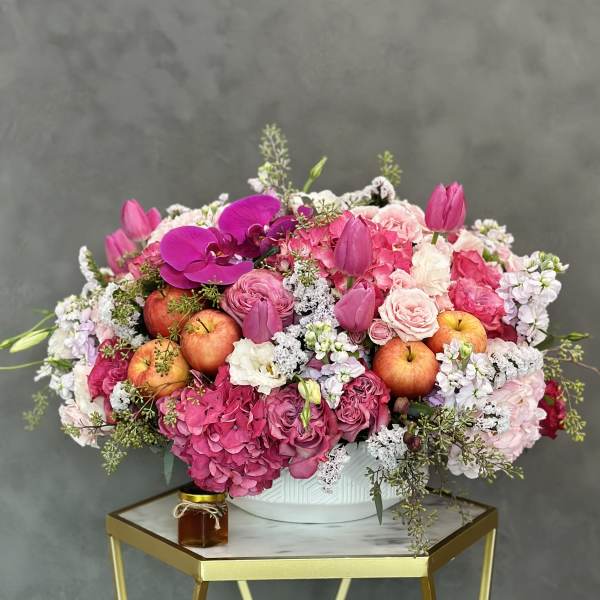 Pink floral arrangement with apples in a white bowl vase