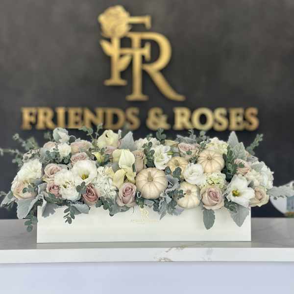 Low floral box arrangement with pale roses, white blooms, and small pumpkins