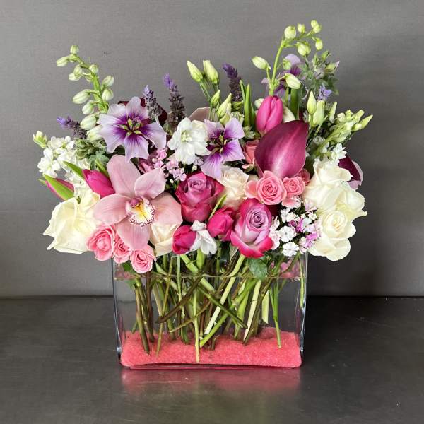 Mixed pink, white, and purple flowers arranged in a clear rectangular vase
