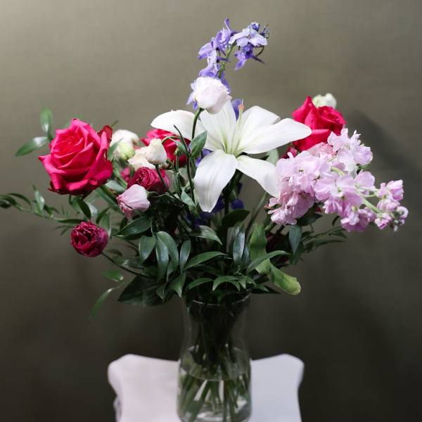 Bouquet of pink roses, white lilies, and lavender flowers in a glass vase