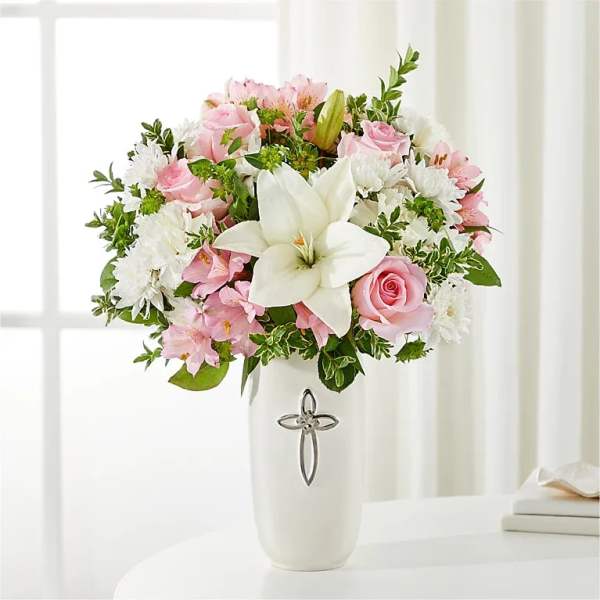 Pink and white floral arrangement in a white vase with a cross emblem