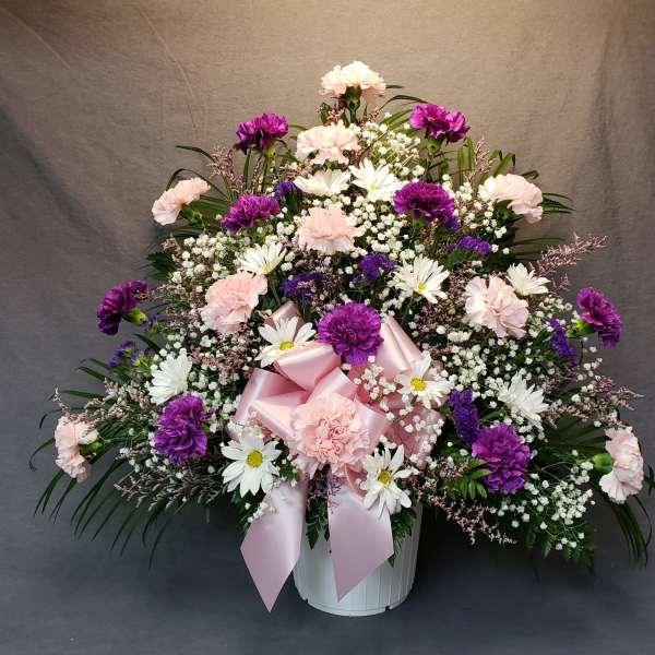 Pink and purple floral arrangement in a white basket with a pink ribbon