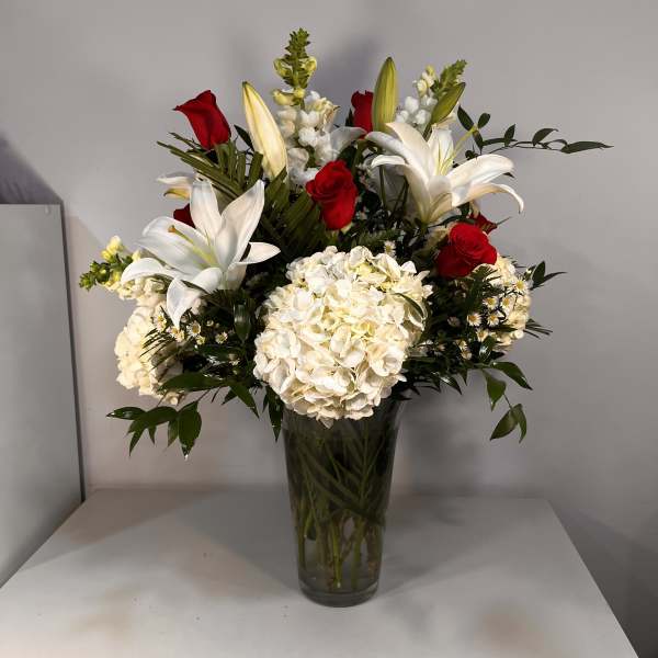 Red roses and white lilies in a tall glass vase with white hydrangeas
