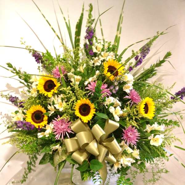 Large mixed bouquet with sunflowers, pink blooms, and a gold ribbon