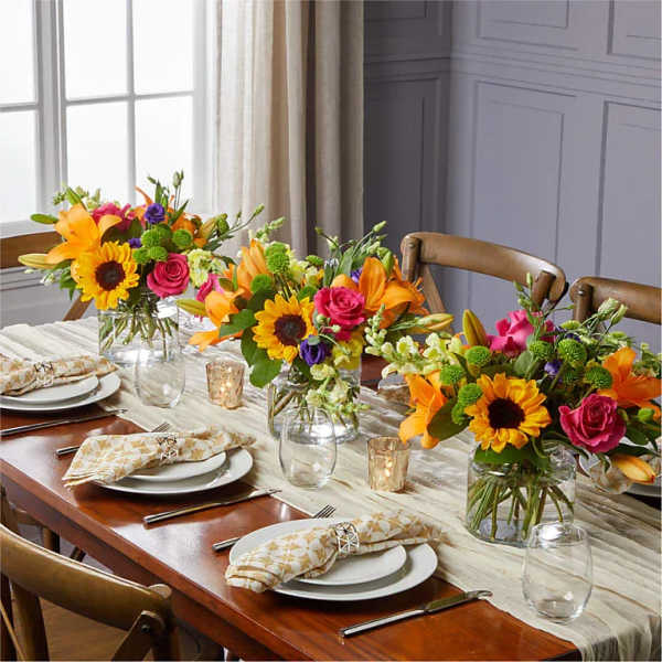 Three colorful floral centerpieces in glass vases on a set dining table