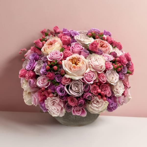 Round bouquet of pink, lavender, and white roses in a gray vase
