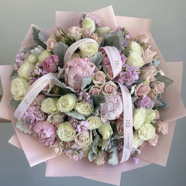 Bouquet of pale pink and cream roses with lavender blooms wrapped in pink paper