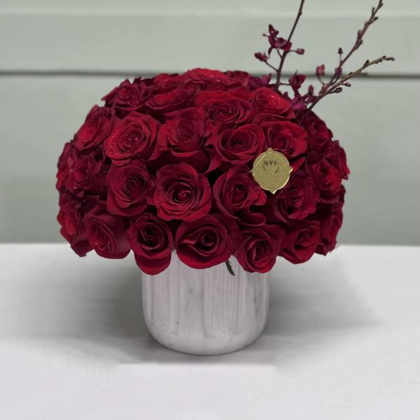 Red rose arrangement in a white vase with decorative branches