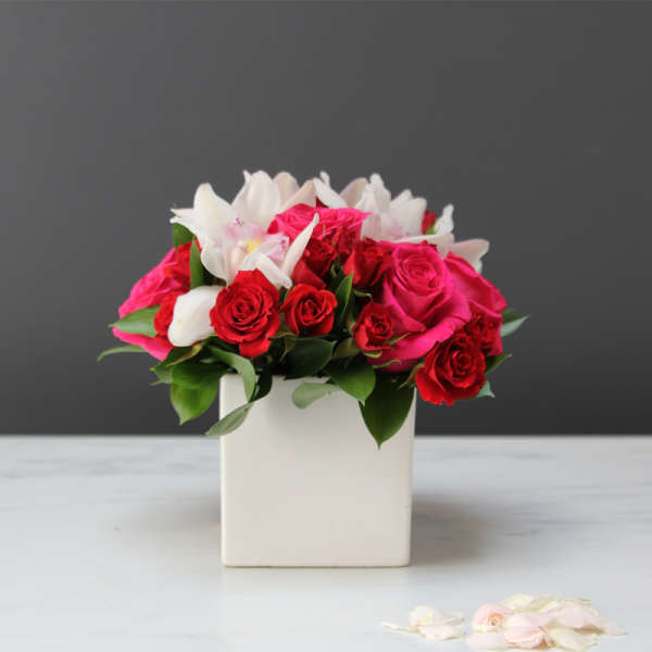 Pink and red roses with white lilies in a white square vase