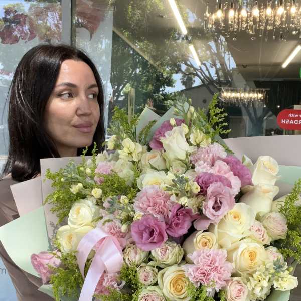 Woman holding a large bouquet of pink and cream flowers with a ribbon