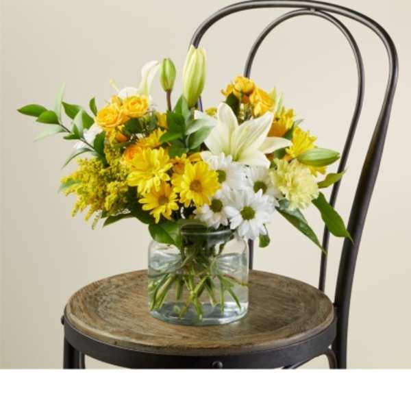 Yellow and white flowers in a clear glass vase on a chair