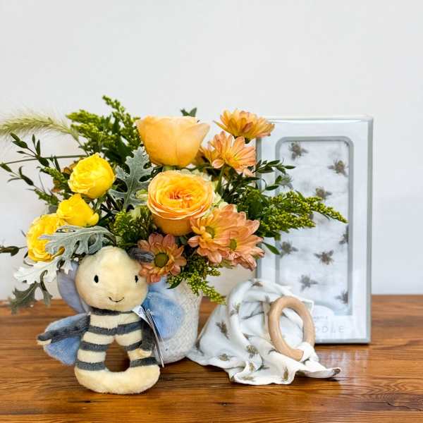 Baby-themed gift set with yellow and peach flowers in a vase, bee plush toy, and bee-print blanket.