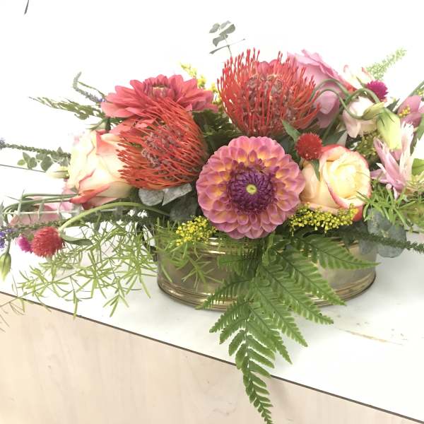 Low floral arrangement with pink, peach, and purple blooms in a shallow container