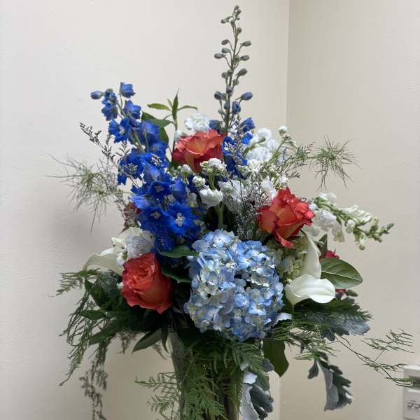Tall mixed bouquet with blue hydrangeas, red roses, and white calla lilies in a glass vase