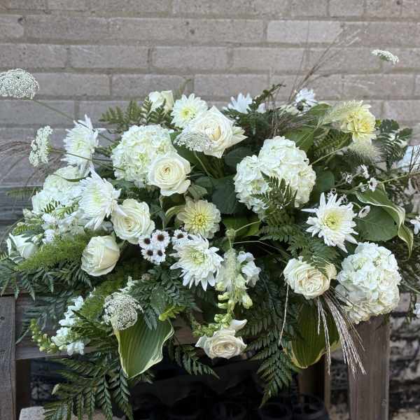 Large white floral arrangement with roses and hydrangeas in a low container