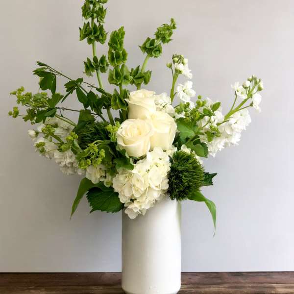 Tall white and green floral arrangement with roses and hydrangeas in a white vase