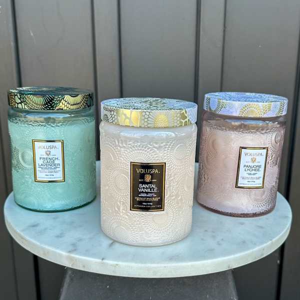 Three large decorative glass jar candles with patterned lids on a round marble stand