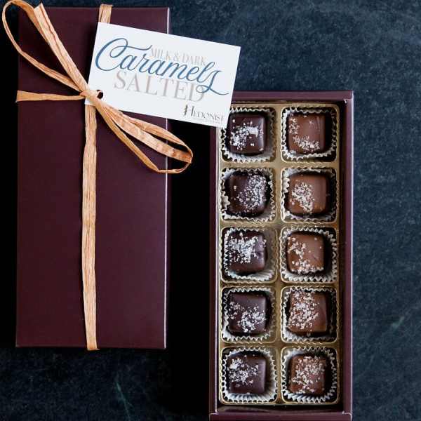 Rectangular gift box of salted caramels with ribbon and open tray showing assorted chocolates.