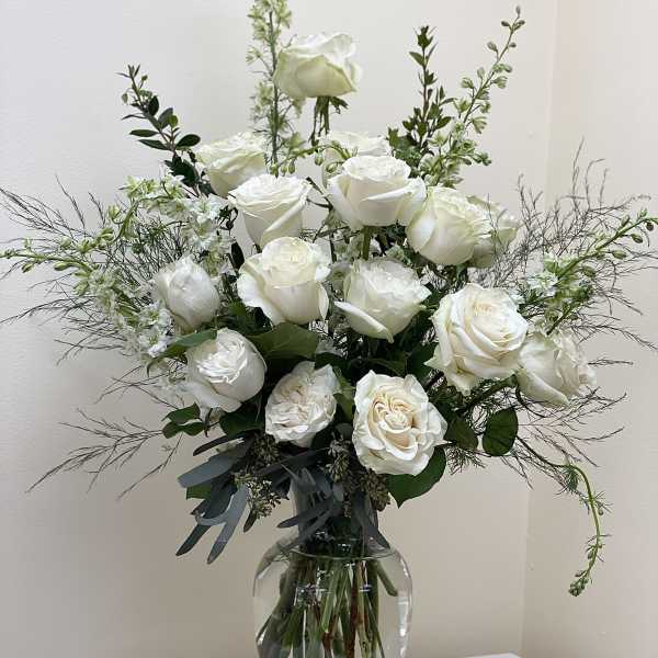 White roses arranged in a clear glass vase with airy greenery