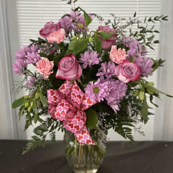 Pink and lavender bouquet in a glass vase with a heart-pattern ribbon