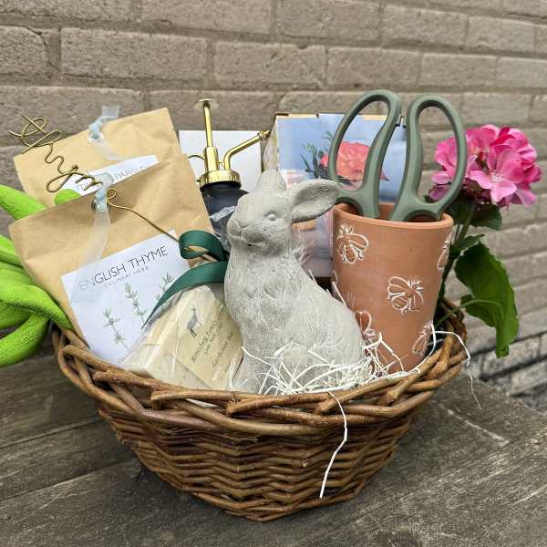 Gift basket with potted pink flowers, herb packets, gloves, and garden tools