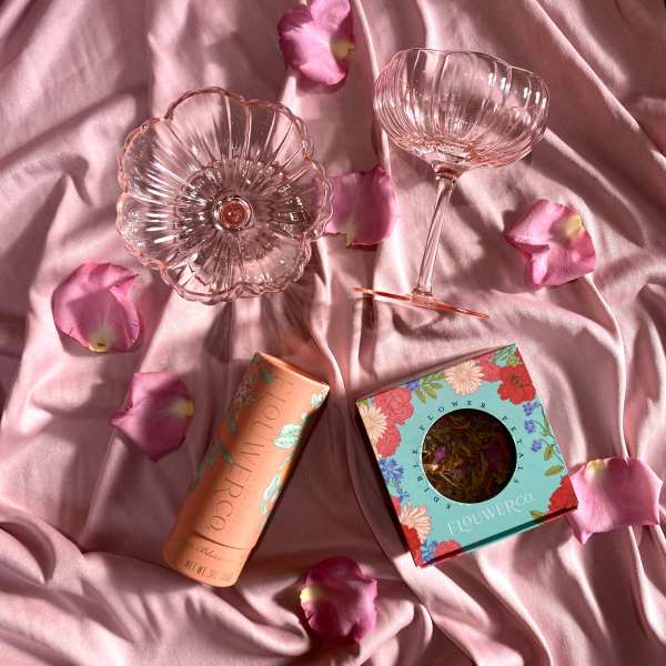 Pink glass coupe and bowl with packaged flower petals on pink fabric with scattered rose petals