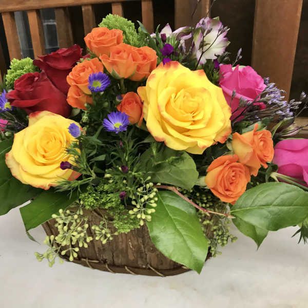 Mixed roses in a low basket arrangement with purple accent flowers